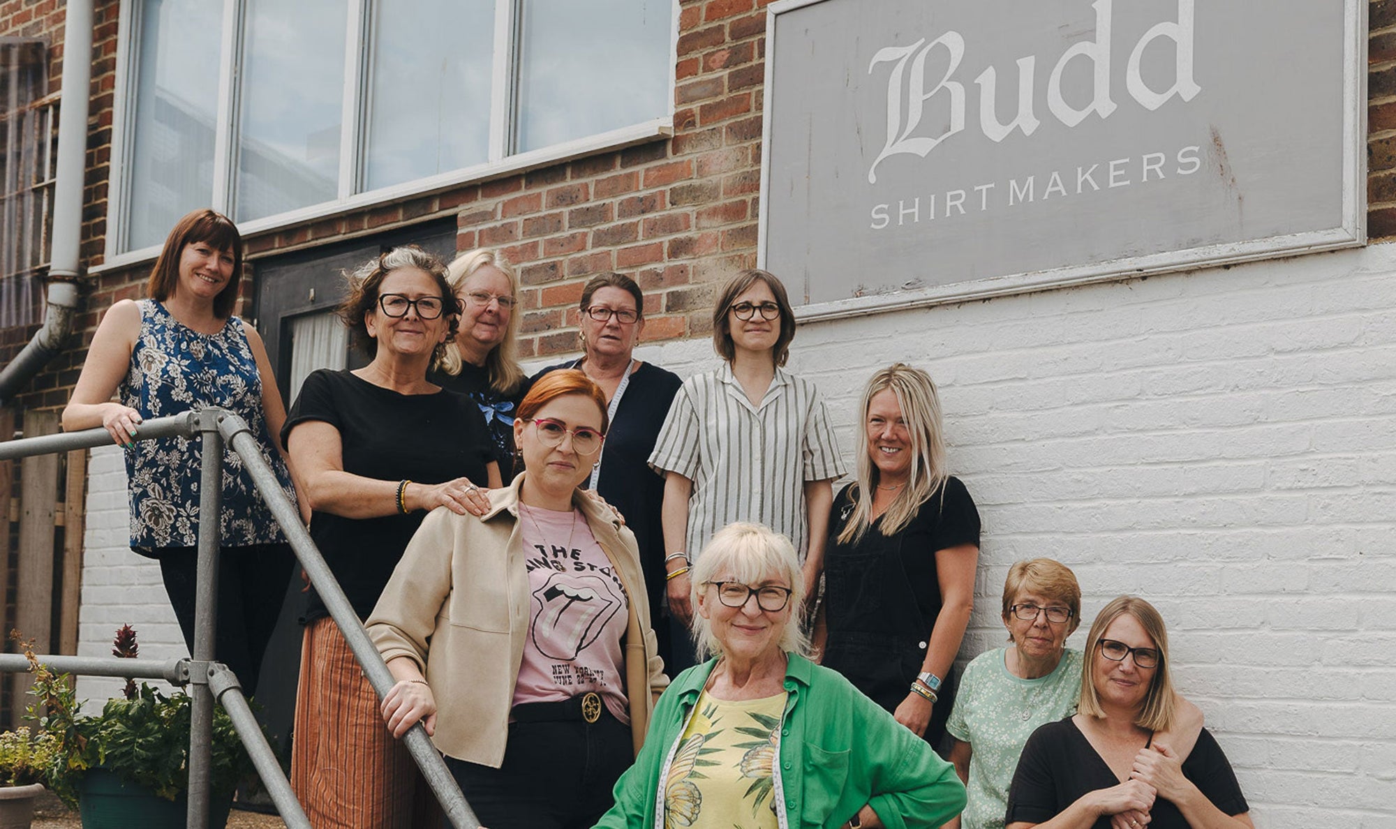 Andover workroom team posing in front of a building with 'Budd Shirtmakers' sign.