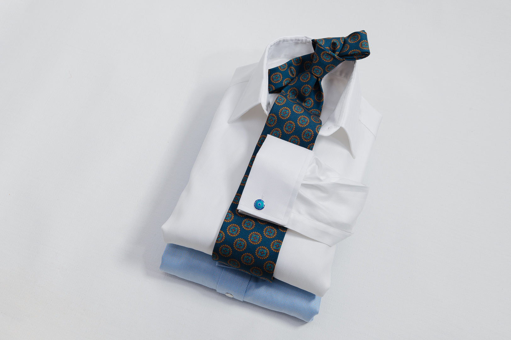 White dress shirt with a blue patterned tie and cufflinks on a light gray background