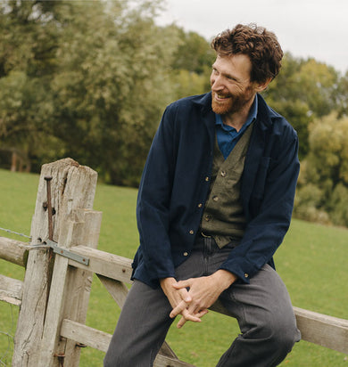 Man sitting on a wooden gate in a field with trees in the background