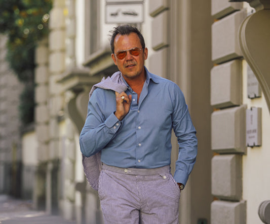 Man wearing demin shirt in blue walking down the street with suit jacket over shoulder
