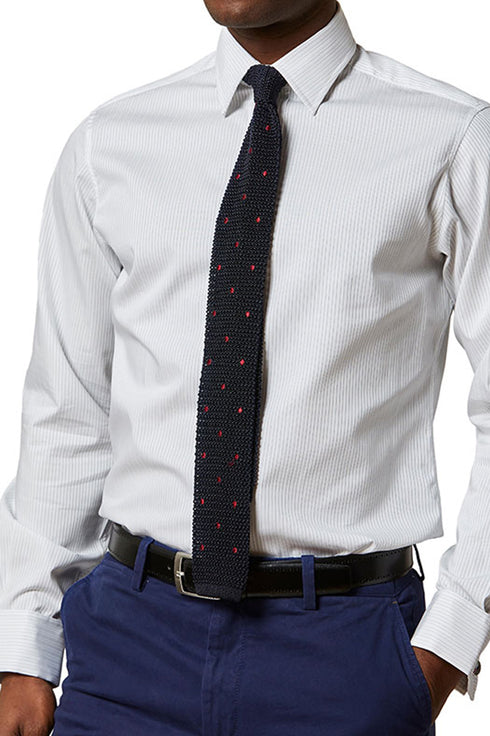 Close up detail of man wearing shirt and knitted polka dot tie with blue trousers 