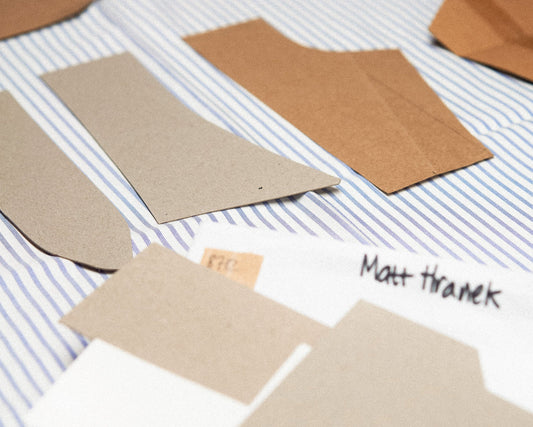 Several brown paper pattern pieces and a white paper template labeled 'Matt Thranek' are arranged on a blue-and-white striped fabric background.
