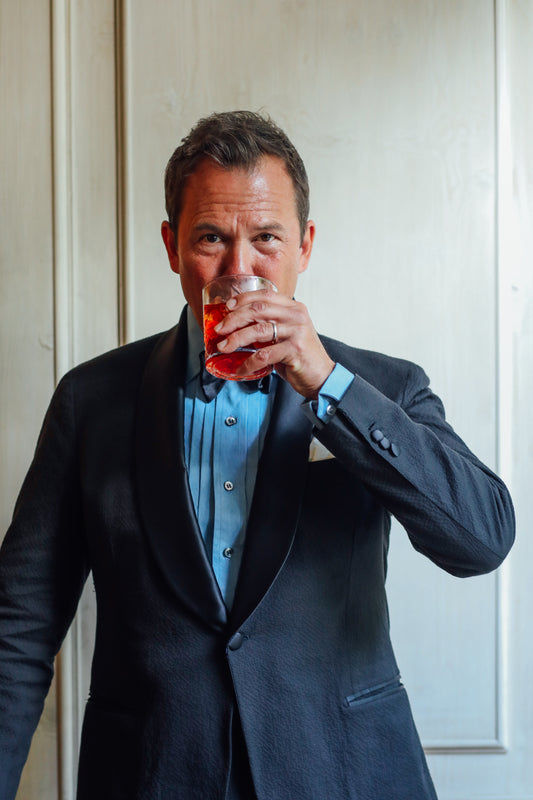 Matt Hranek drinking a Negroni whilst wearing a WM BRown x Budd washed blue denim pleated front dress evening shirt with cocktail cuff 