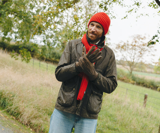 Man wearing a red beanie, scarf, and gloves standing outdoors in a natural setting.