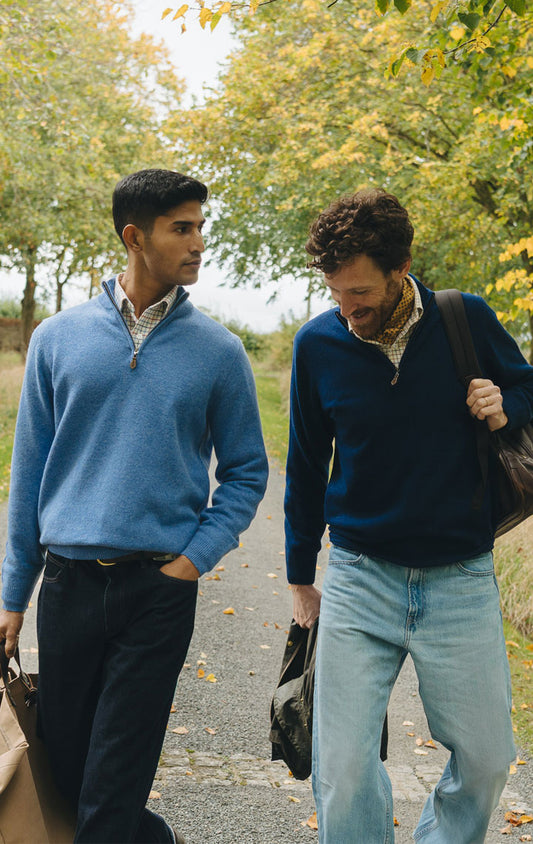 Two men wearing blue sweaters walking outdoors with trees in the background
