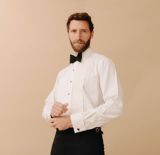 Man wearing black tie attire stood against plain peach coloured background