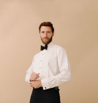 Man wearing black tie attire stood against plain peach coloured background
