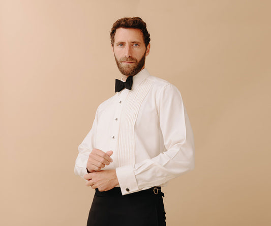 Man wearing black tie attire stood against a peach coloured plain background