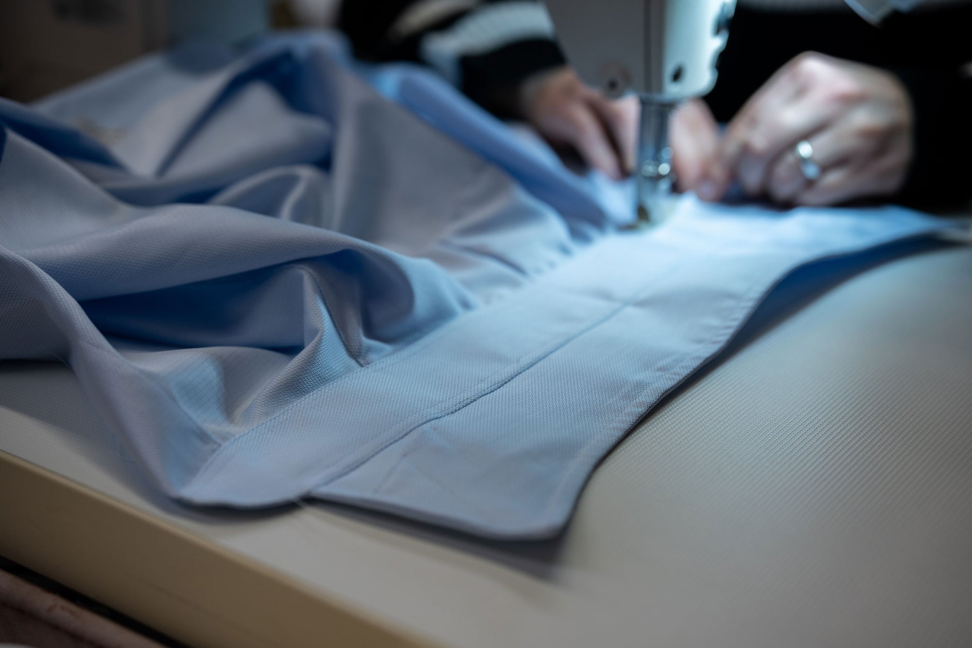Close up of blue shirt being made by a sewing machine