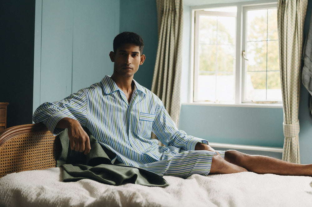 Male model laid on bed wearing a blue striped nightshirt