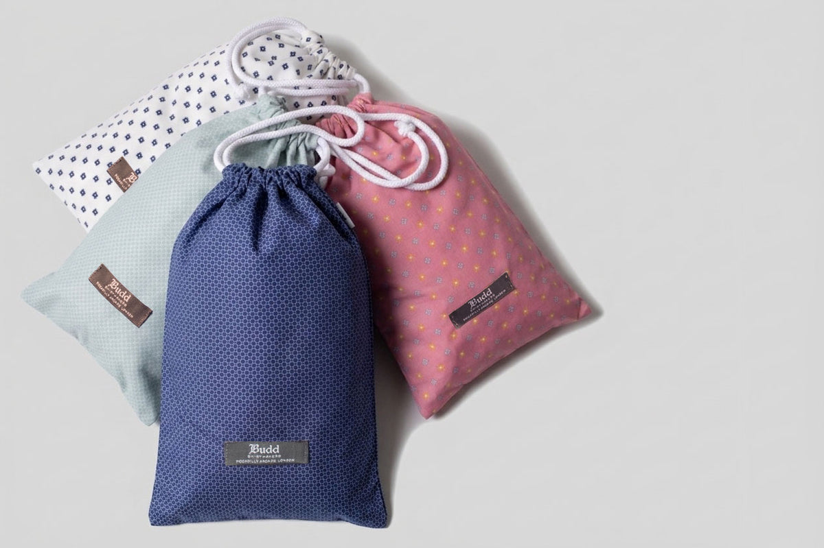 Four drawstring swim shorts bags in blue, pink, and white with polka dot patterns on a light gray background.