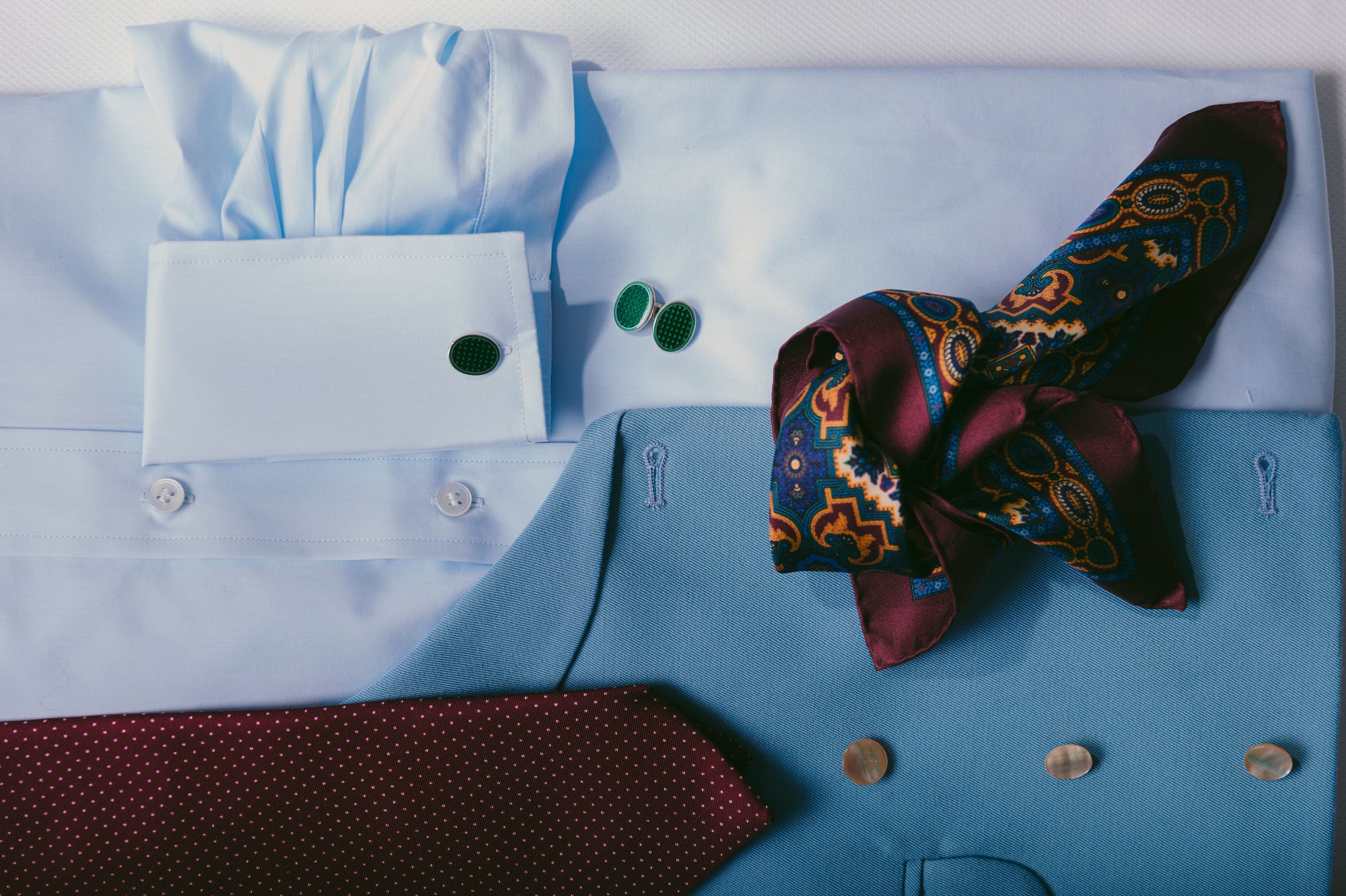 Blue shirt with a red patterned tie, pocket square, and cufflinks on a white background
