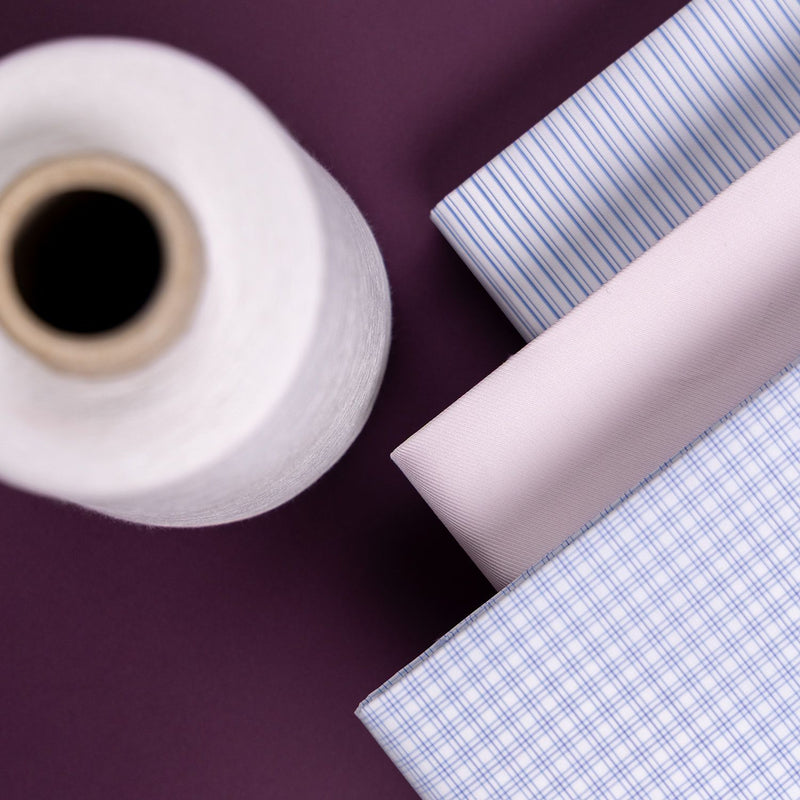 Roll of white fabric and three different patterned fabrics on a purple background