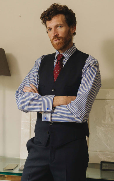 Man wearing a striped shirt, vest, and tie with arms crossed indoors.