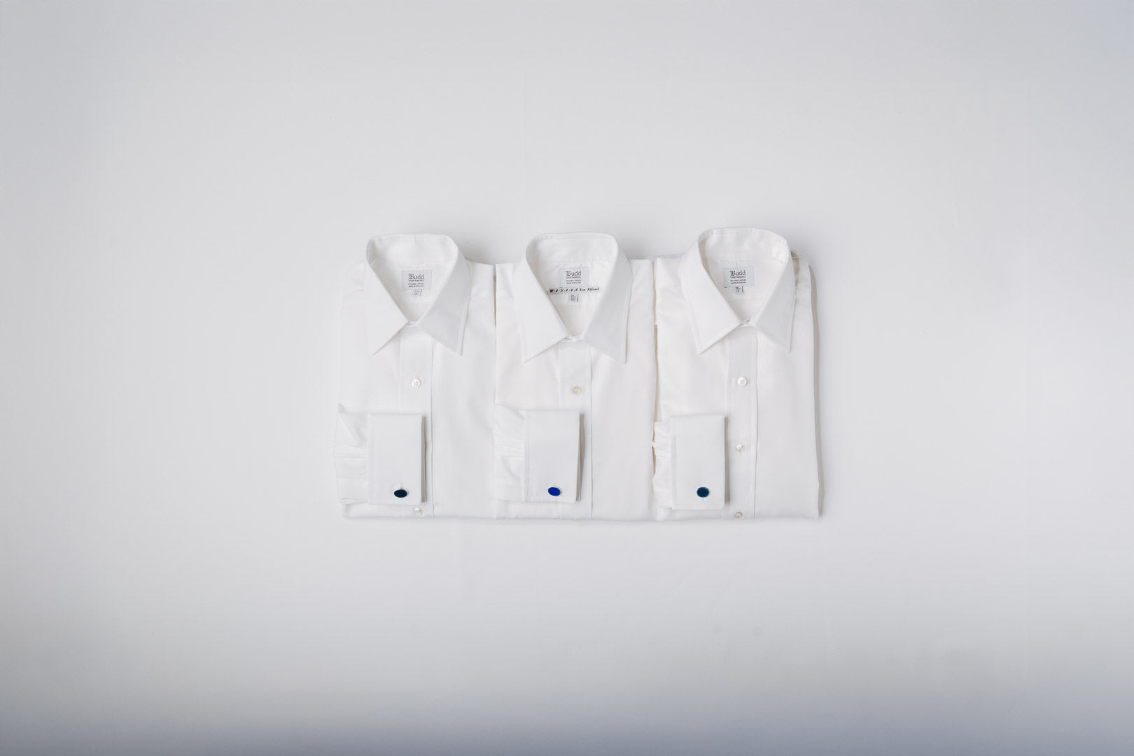 Three white dress shirts with cufflinks on a light gray background