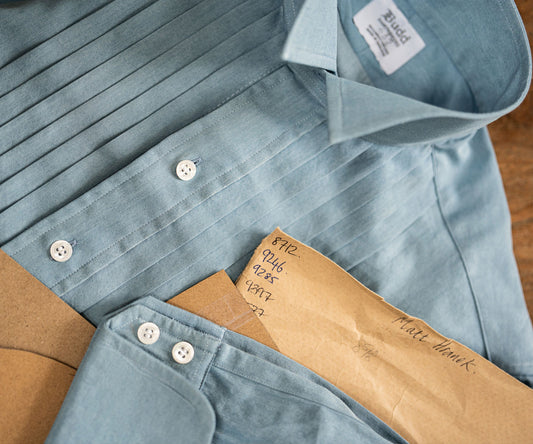 Pleated denim shirt in blue laid out on wooden table 
