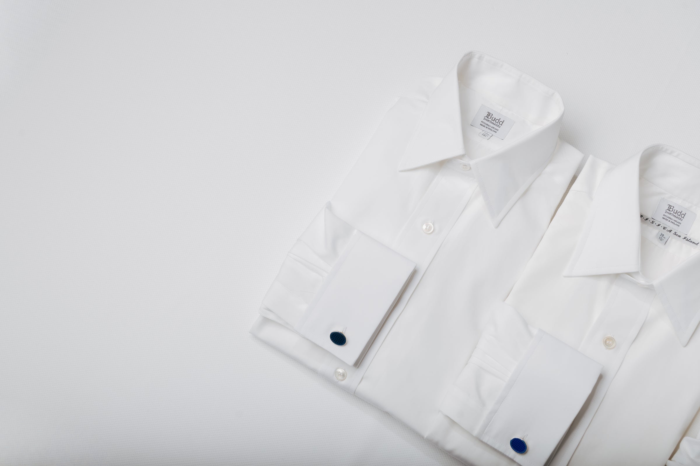 Two white shirts laid out on white background