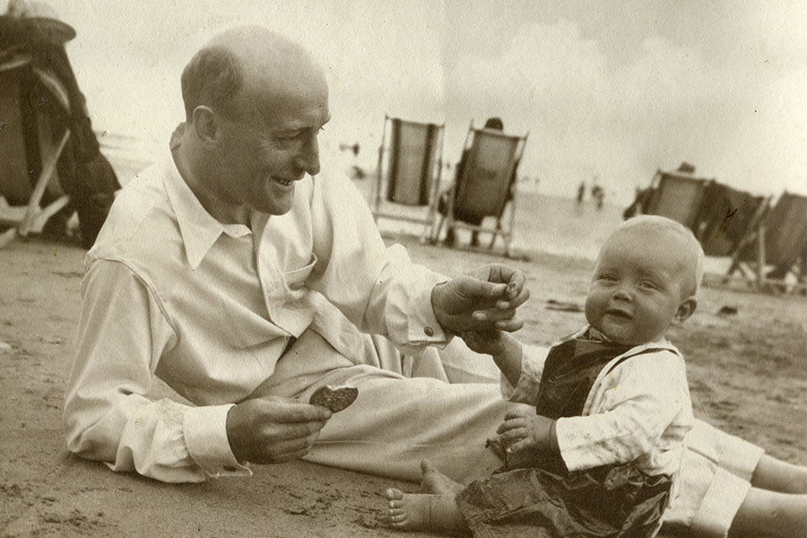 Man and child sitting on a beach with deck chairs in the background